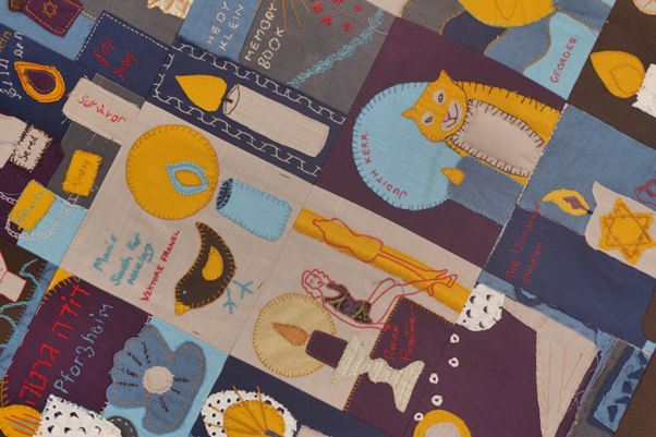 Photograph of a collaboratively embroidered and appliques patchwork quilt representing 80 individuals affected by the Nazi regime.